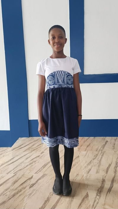A student wearing the formal uniform for girls, showing the Ndop waist panel and the patterned hem border